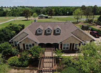 Aerial drone view of completed shingle roof replacement on large brick home near Tyler, TX